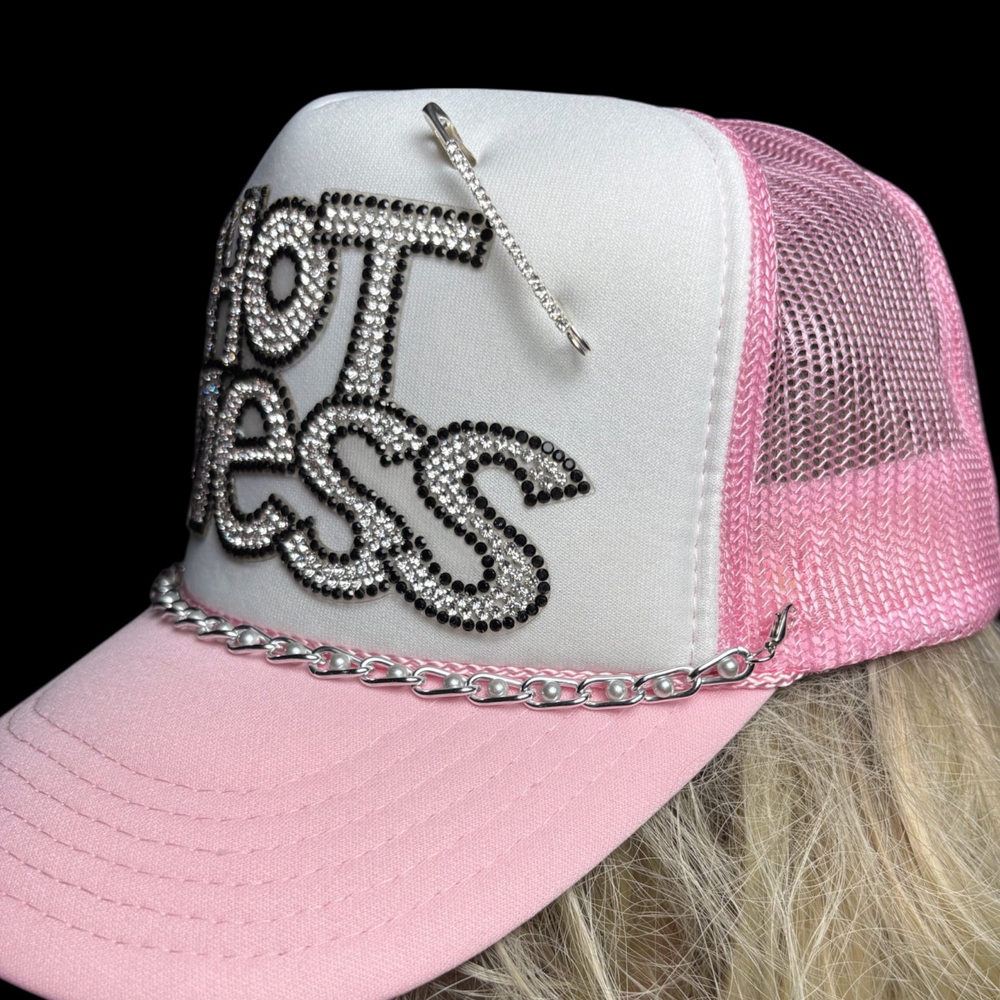 Pink and white cap with rhinestone text and chains on a black background